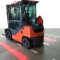Industrial vehicle using TYRI VL4 RedLine LED lights to project clear red boundary lines on the floor, creating a visual safety zone around the machine in a warehouse setting.