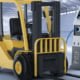 An Electric Forklift Truck stands in a warehouse where it is plugged into a charging point.
