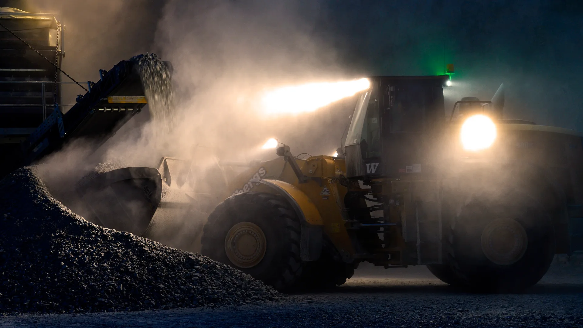 A wheel loader works on a construction site at night using its TYRI work lights to light the surrounding area creating a safe and efficient workspace.