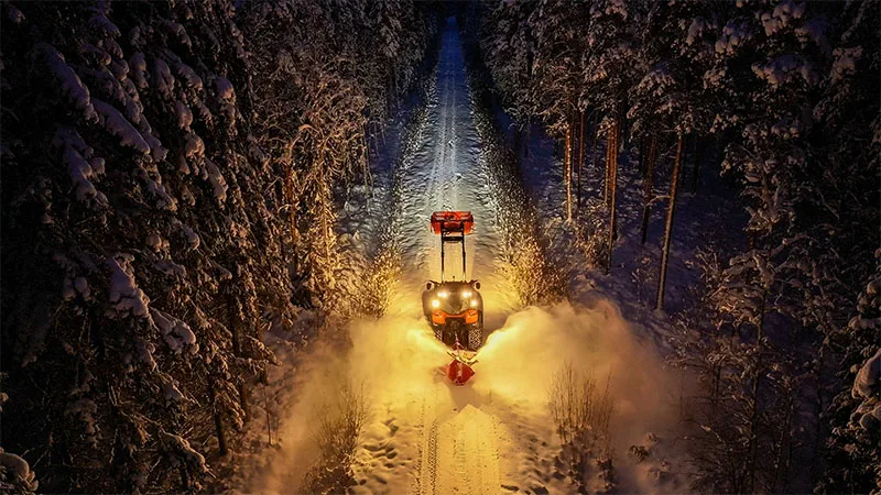 TYRIINTELLiLight 作業灯を装着したValtra Unlimitedトラクターが、夕暮れの険しい田園風景の中で作業し、農作業や畑仕事に強力な照明を提供している。