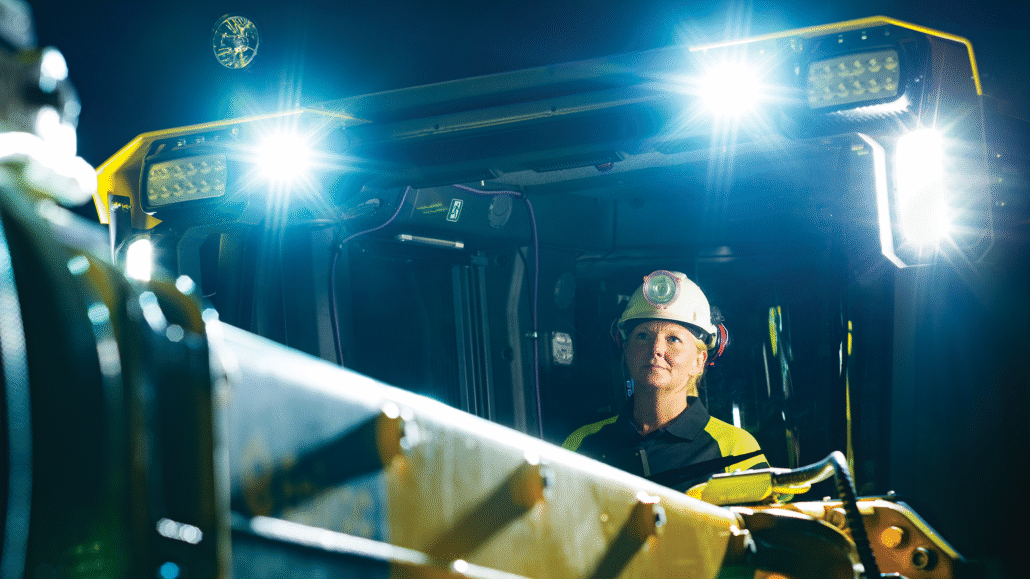 Female operator inside the Epiroc Boomer M20 Battery drill rig cabin illuminated by TYRI 1323 and 1313 LED work lights, highlighting safe, sustainable underground mining technology.