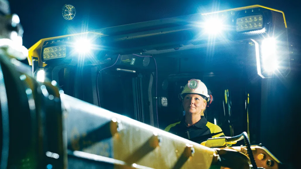 Female operator inside the Epiroc Boomer M20 Battery drill rig cabin illuminated by TYRI 1323 and 1313 LED work lights, highlighting safe, sustainable underground mining technology.