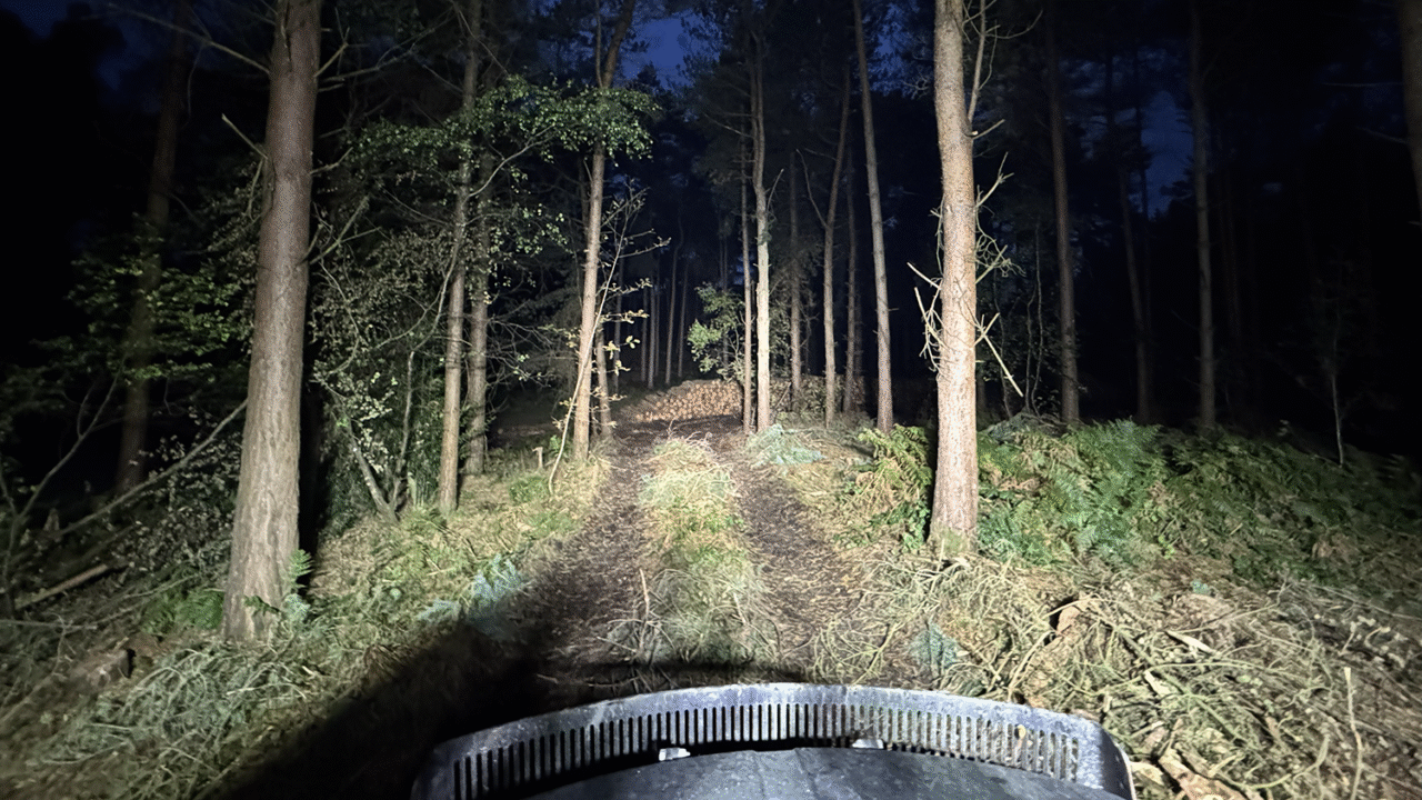Nighttime forest work scene illuminated by TYRI LED work lights from a forestry forwarder, lighting up a woodland trail for logging operations and improved operator visibility