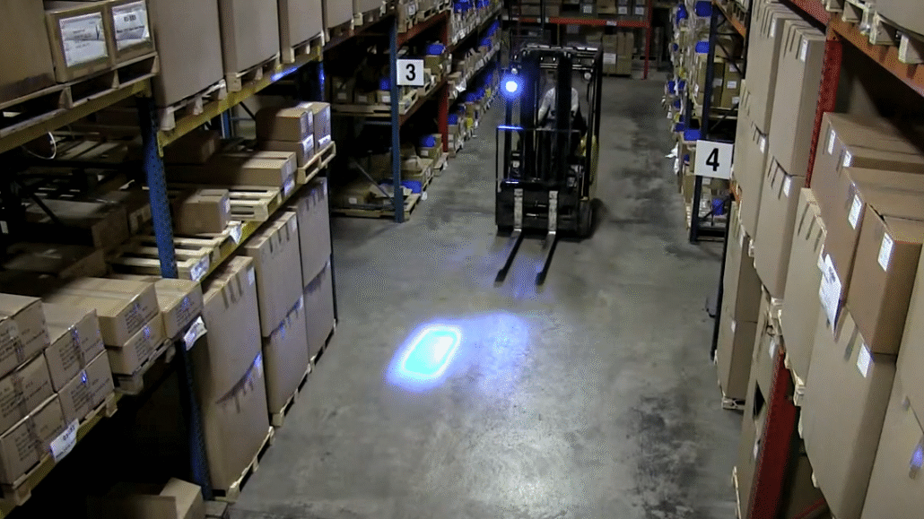 Forklift equipped with TYRI 1010 BluePoint LED safety light projecting a bright blue warning zone on the warehouse floor to alert pedestrians and enhance workplace safety